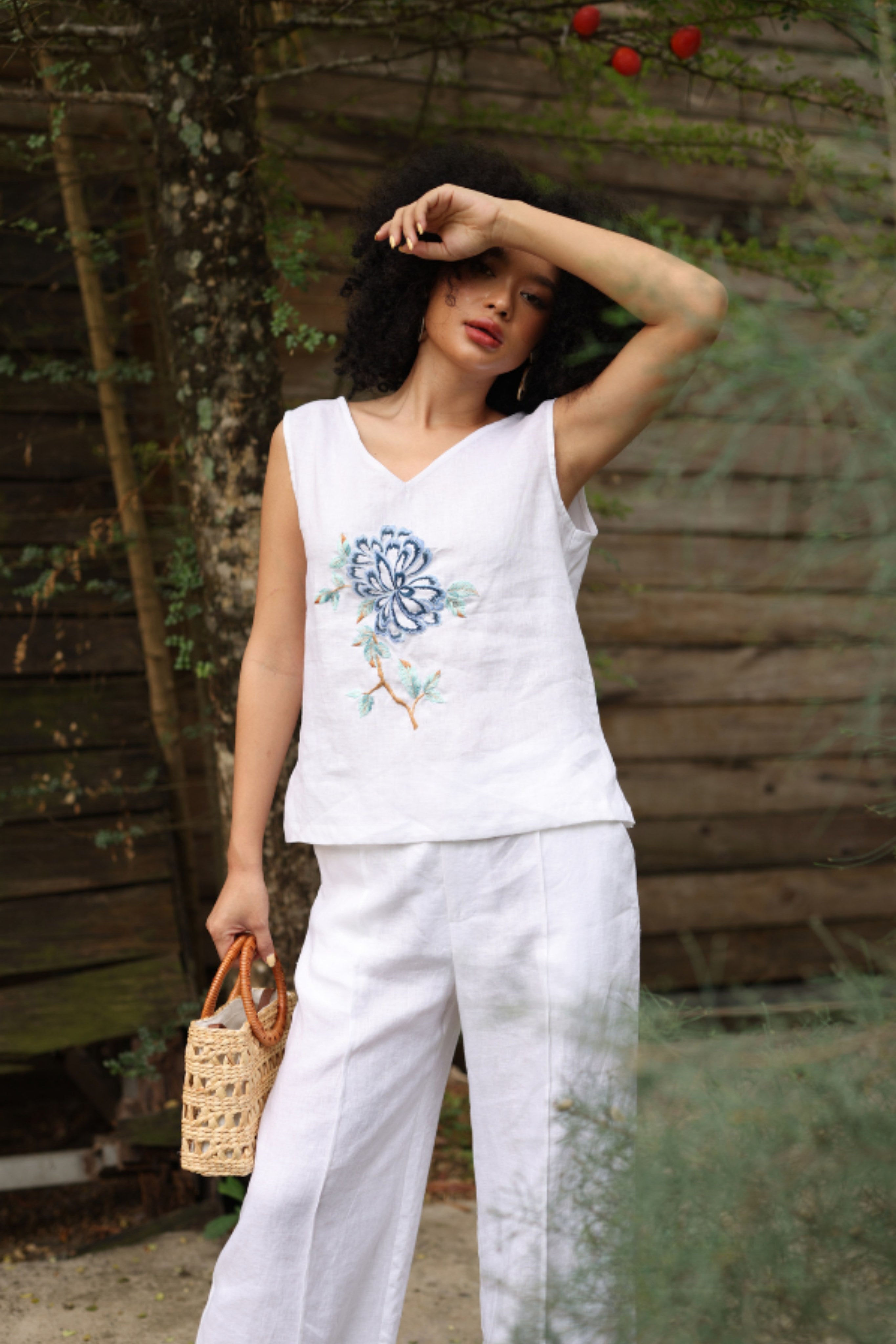 Woman wearing a white sleeveless top with floral design and white pants, standing outdoors.
