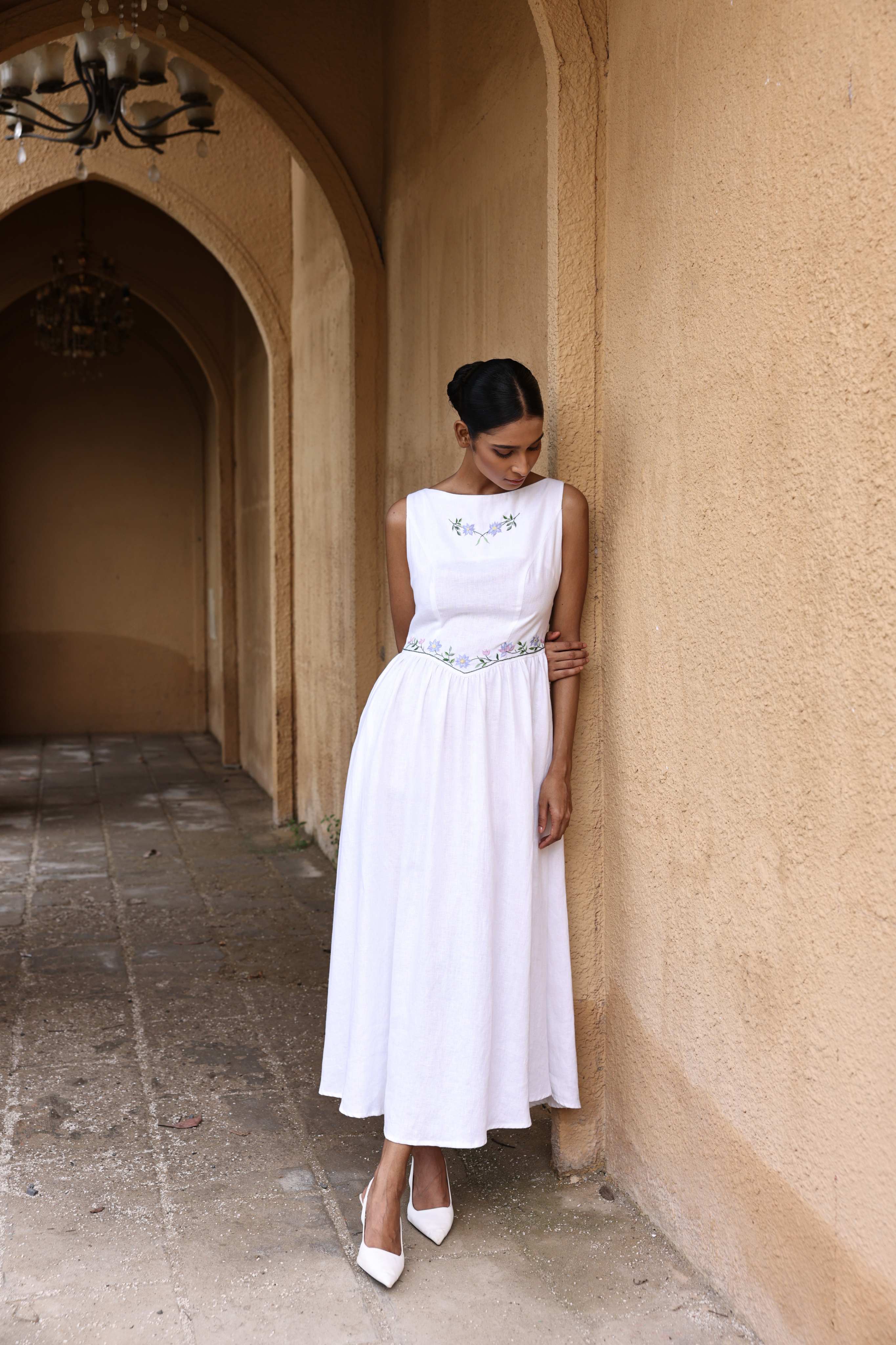 Woman in a white dress standing in a sunlit hallway with arches.
