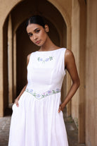 Woman wearing a white dress with floral embroidery in an arched doorway.