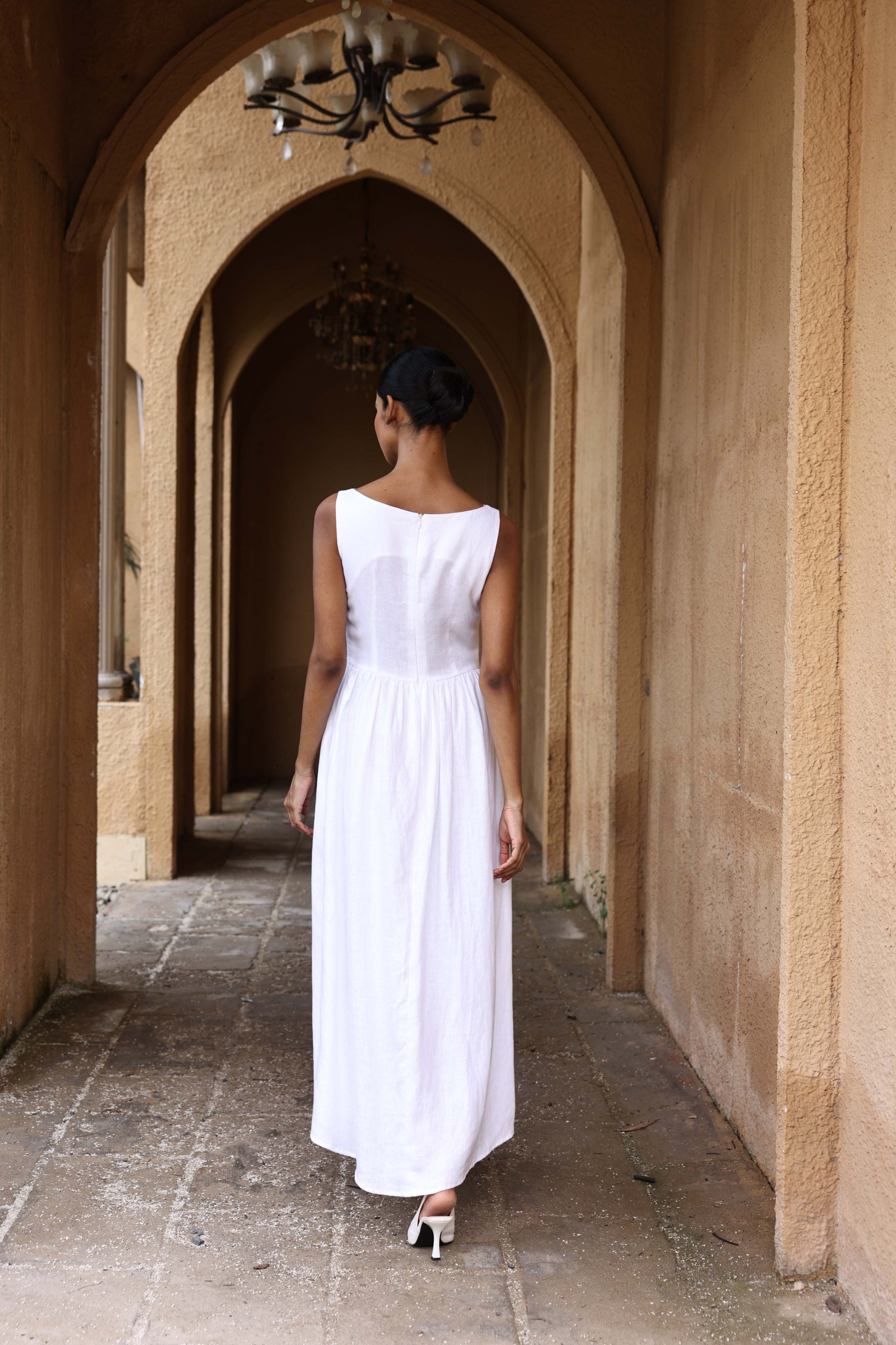 Woman in a white dress walking through an arched stone corridor.