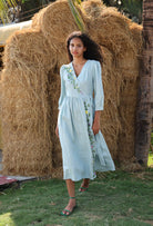 Woman in a light blue dress standing in front of a large hay bale.