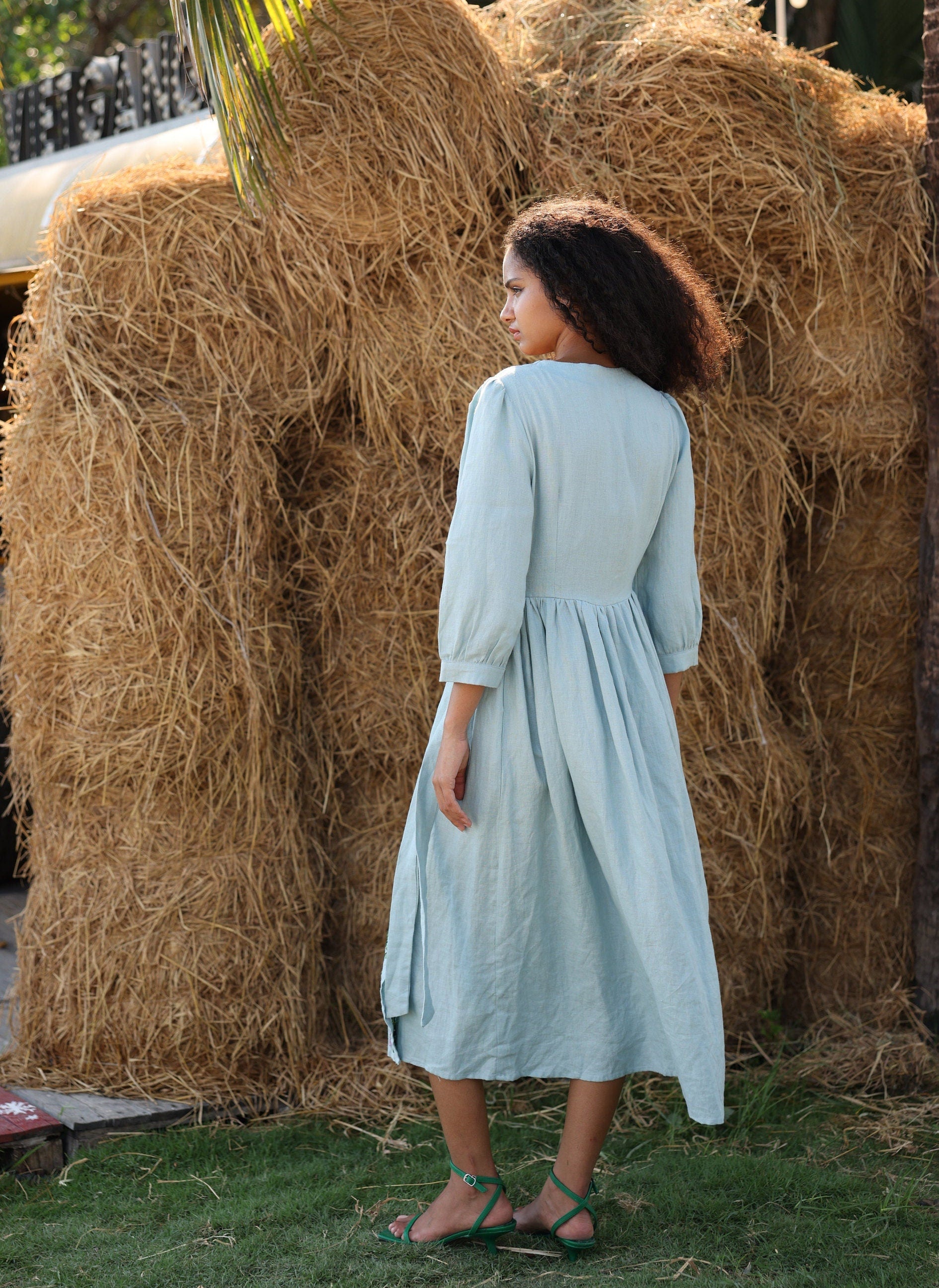 Woman in a light blue dress standing in front of hay bales