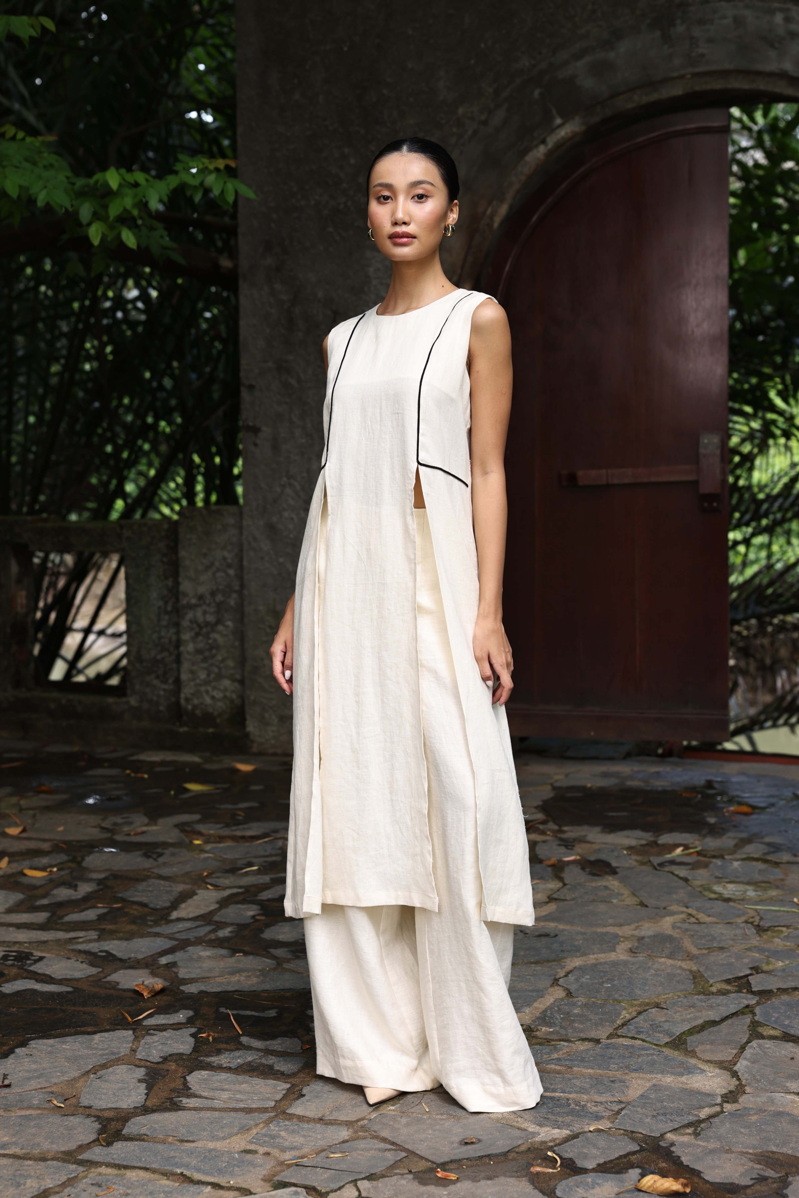 Woman in a white outfit standing on a stone path with greenery in the background
