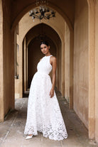 Woman in a white lace dress standing in an arched corridor.