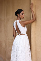 Woman in a white lace dress standing against a beige wall