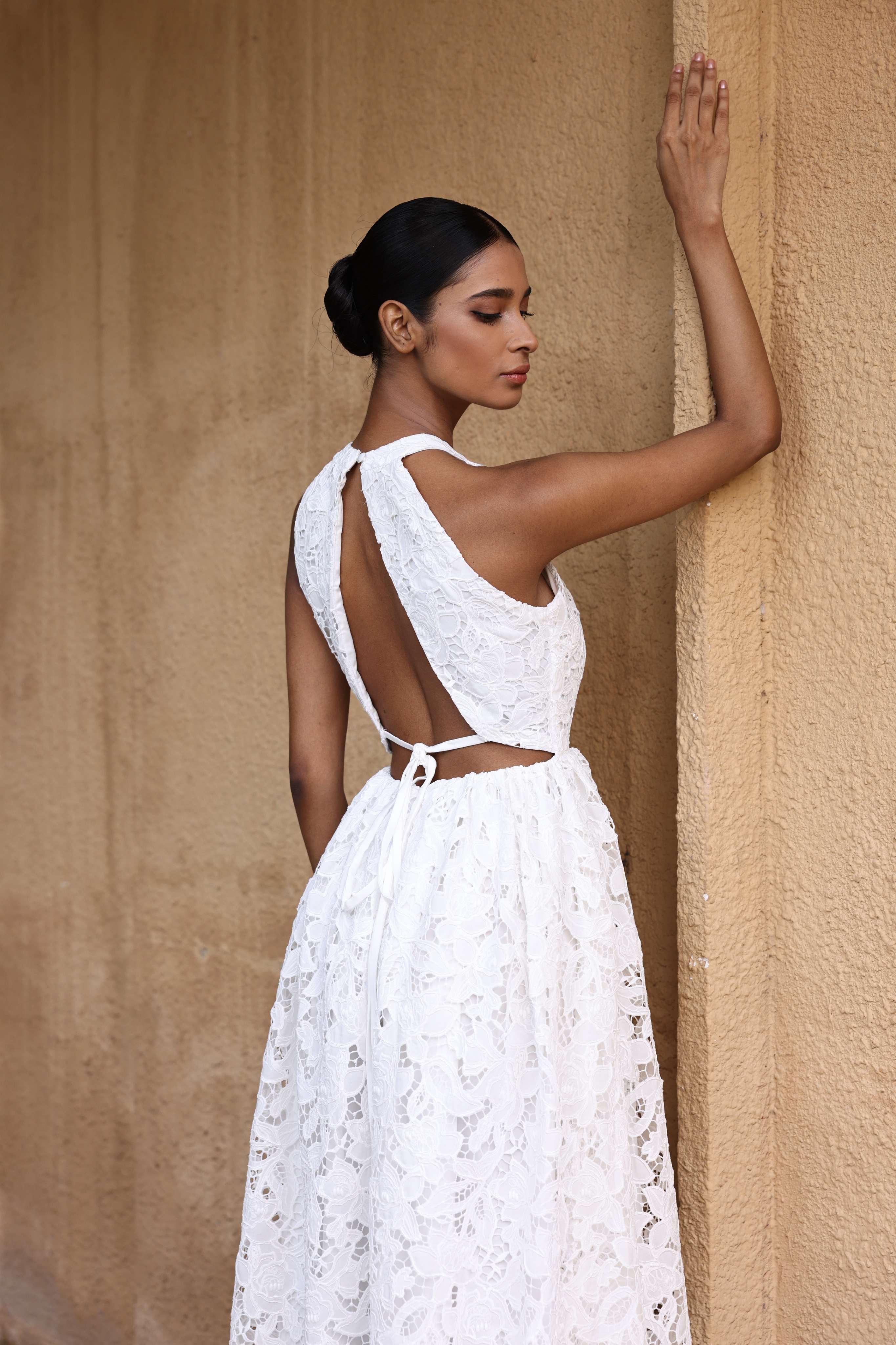 Woman in a white lace dress standing against a beige wall