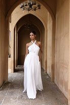 Woman in a white dress standing in an arched hallway with beige walls.