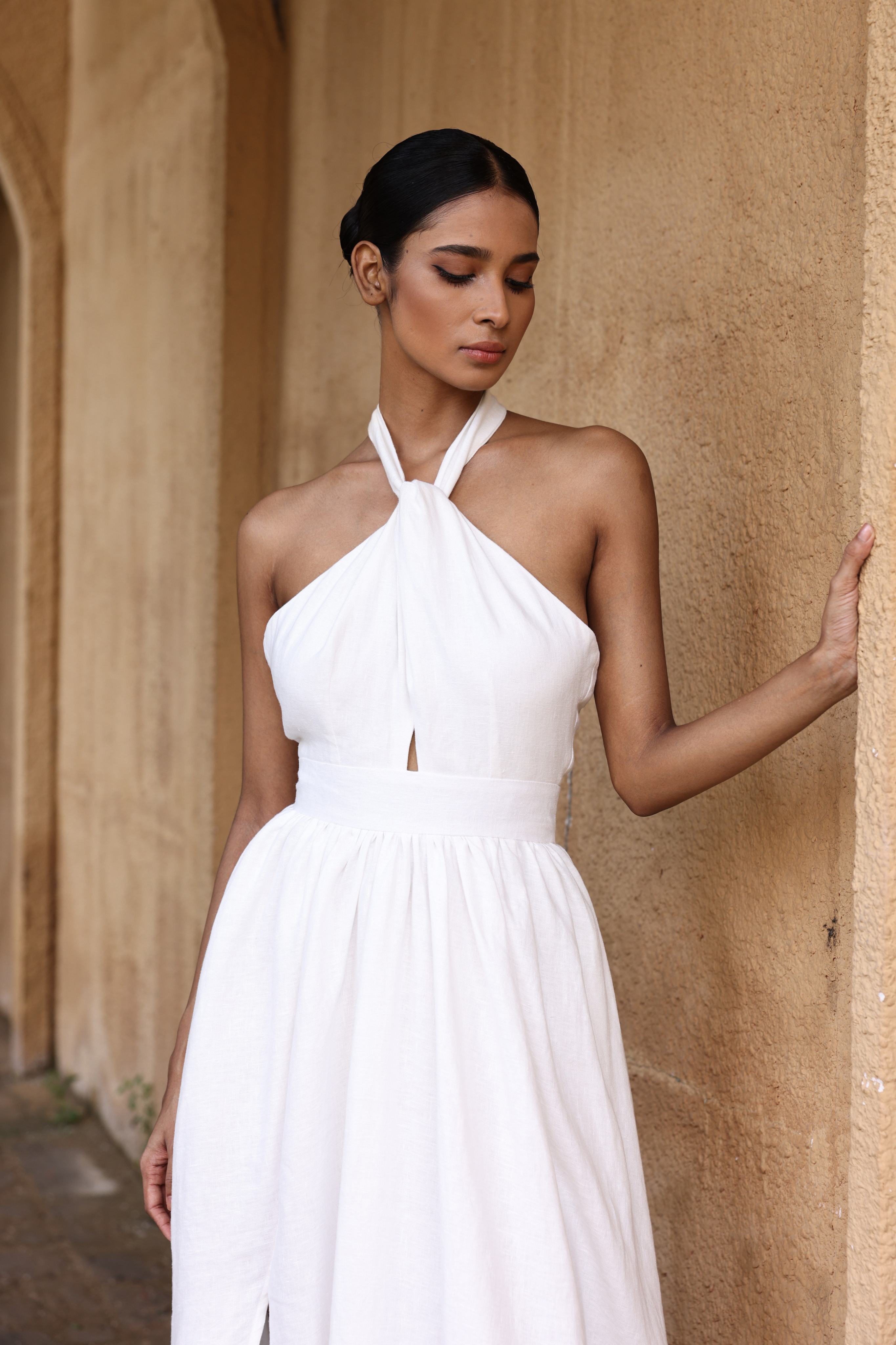 Woman wearing a white halter neck dress against a beige wall.