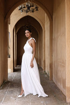 Woman in a white dress standing in an arched hallway with beige walls.