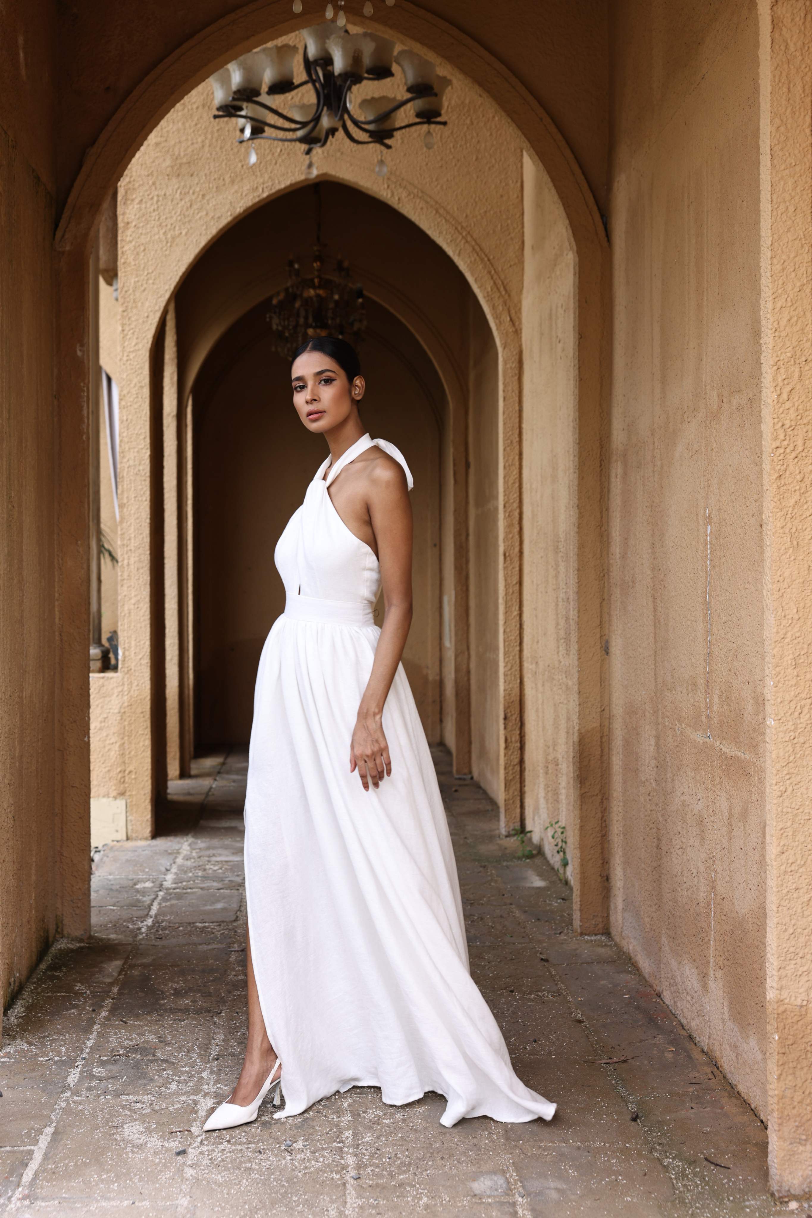 Woman in a white dress standing in an arched hallway with beige walls.
