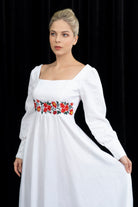 Woman wearing a white dress with floral embroidery on a black background