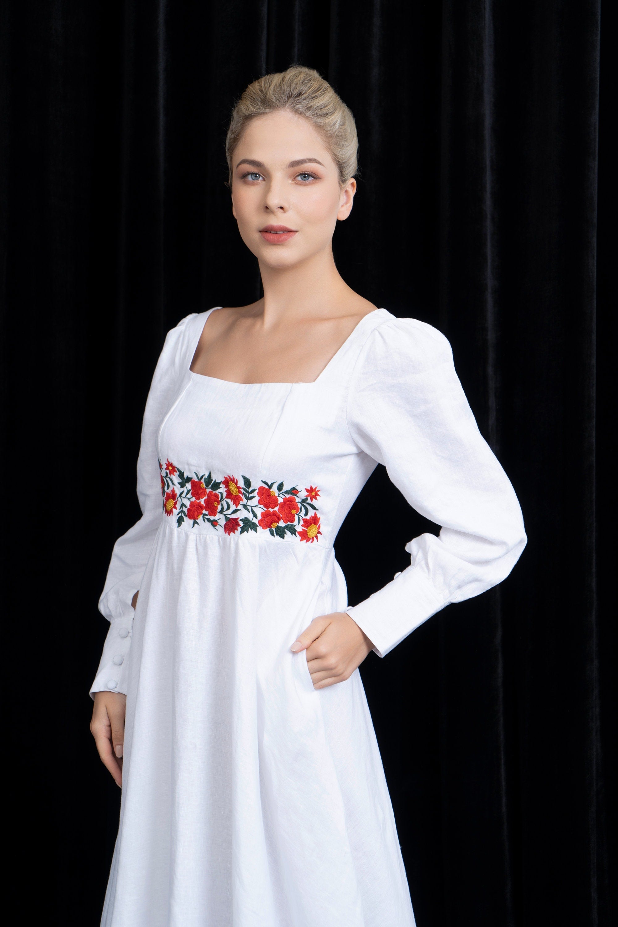 Woman wearing a white dress with floral embroidery against a black background
