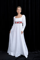 Woman wearing a white dress with floral embroidery on a black background