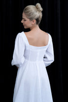 Woman wearing a white dress with long sleeves against a black background
