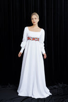 Woman wearing a white dress with floral embroidery on a black background