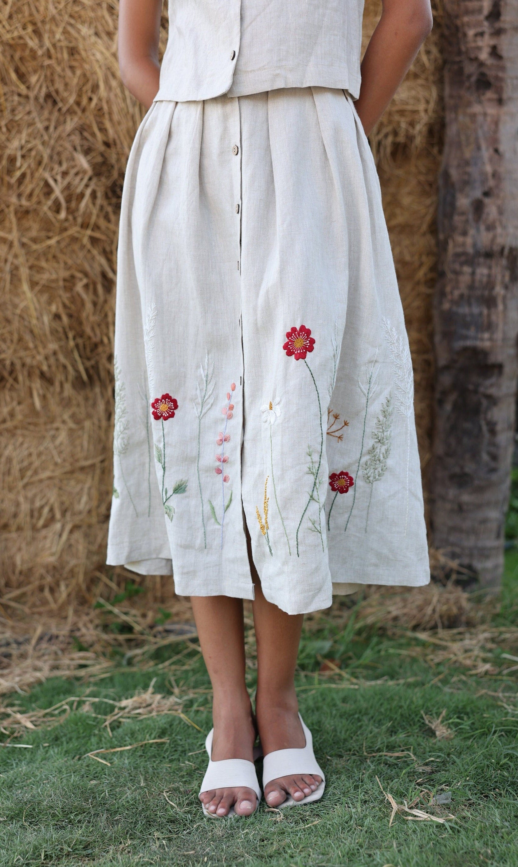 Person wearing a light-colored skirt with floral embroidery standing in a natural setting.