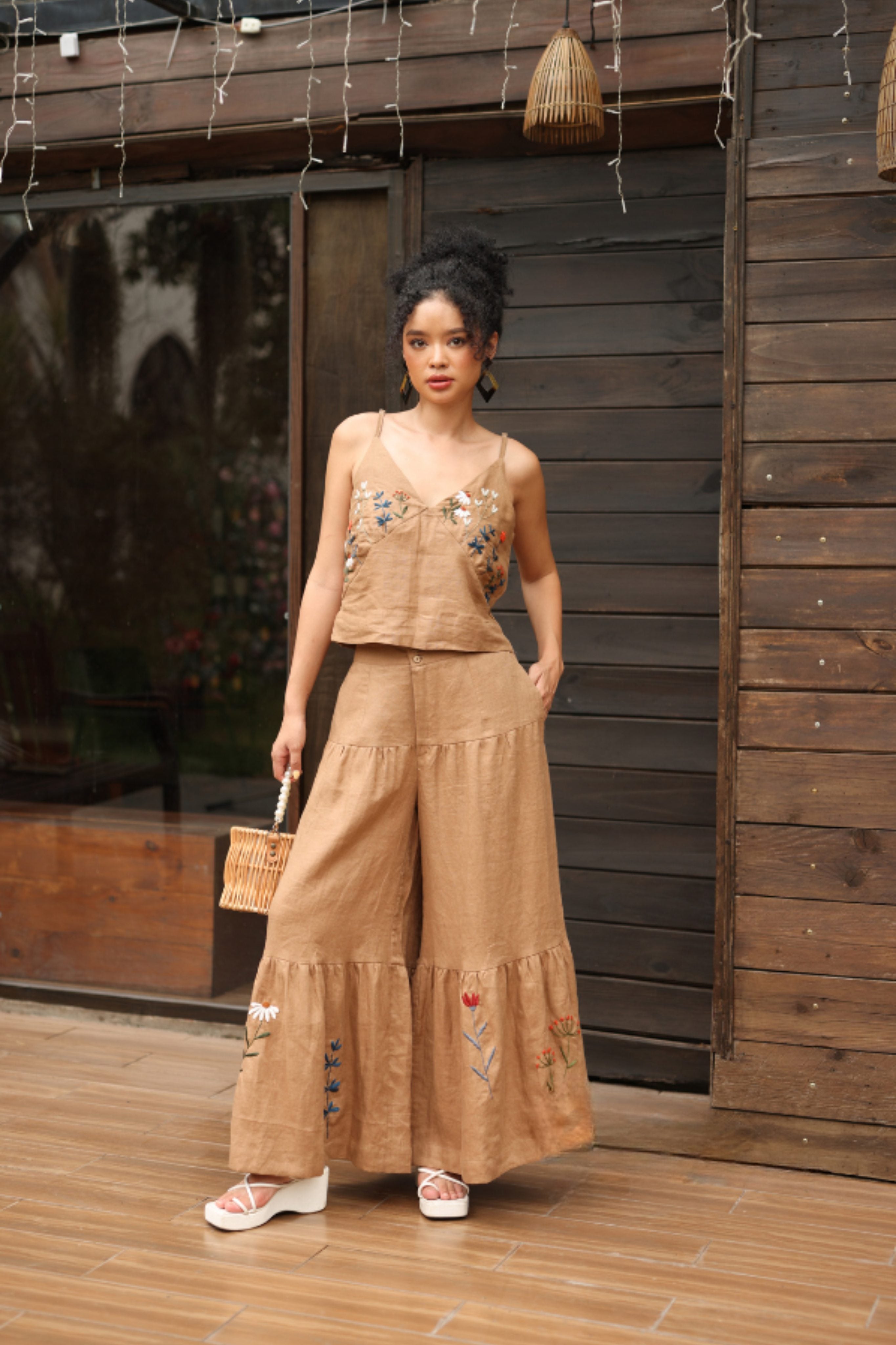 Woman wearing a beige embroidered outfit standing in front of a wooden wall.