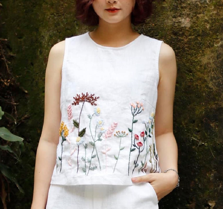 Person wearing a white sleeveless top with floral embroidery against a natural background