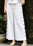Person wearing white pants with buttons against a dark wall.