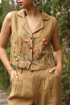 Person wearing a brown sleeveless top with floral embroidery and matching pants outdoors.
