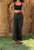 Woman wearing a black crop top and wide-leg pants standing in front of hay bales.