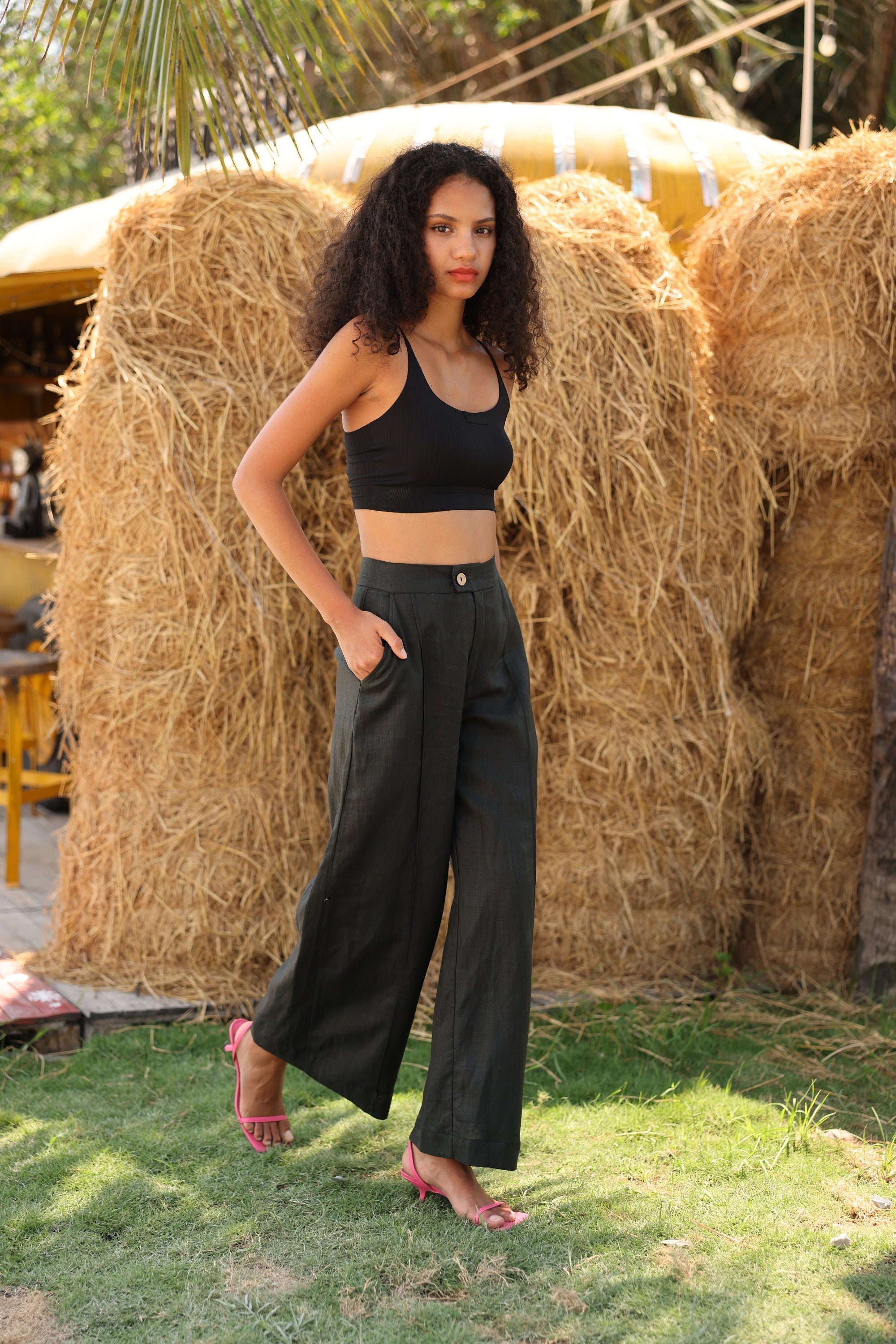 Woman in black top and wide-leg pants standing in front of hay bales outdoors