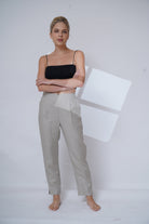 Woman wearing a black top and light gray pants against a white background