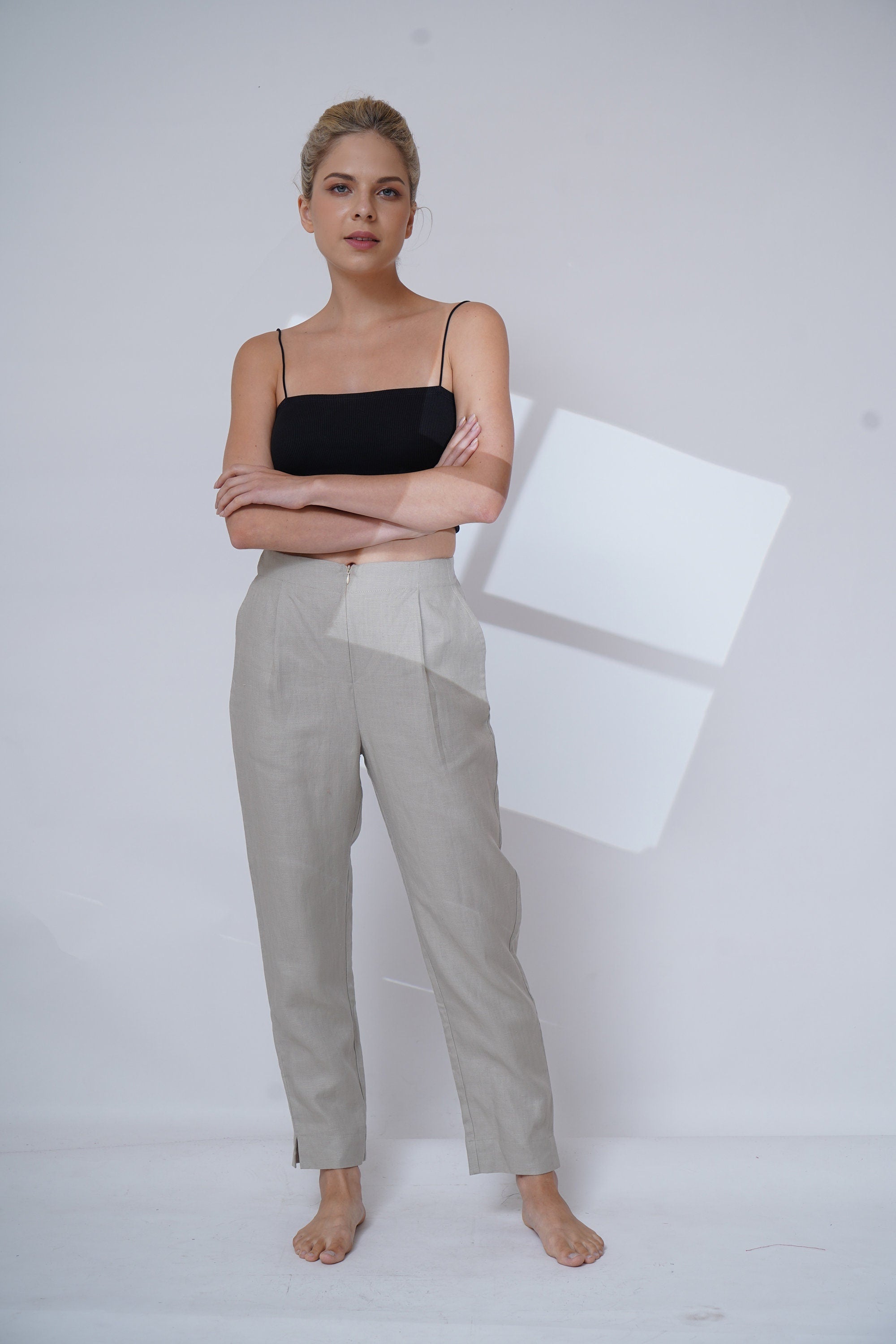 Woman wearing a black top and light gray pants against a white background