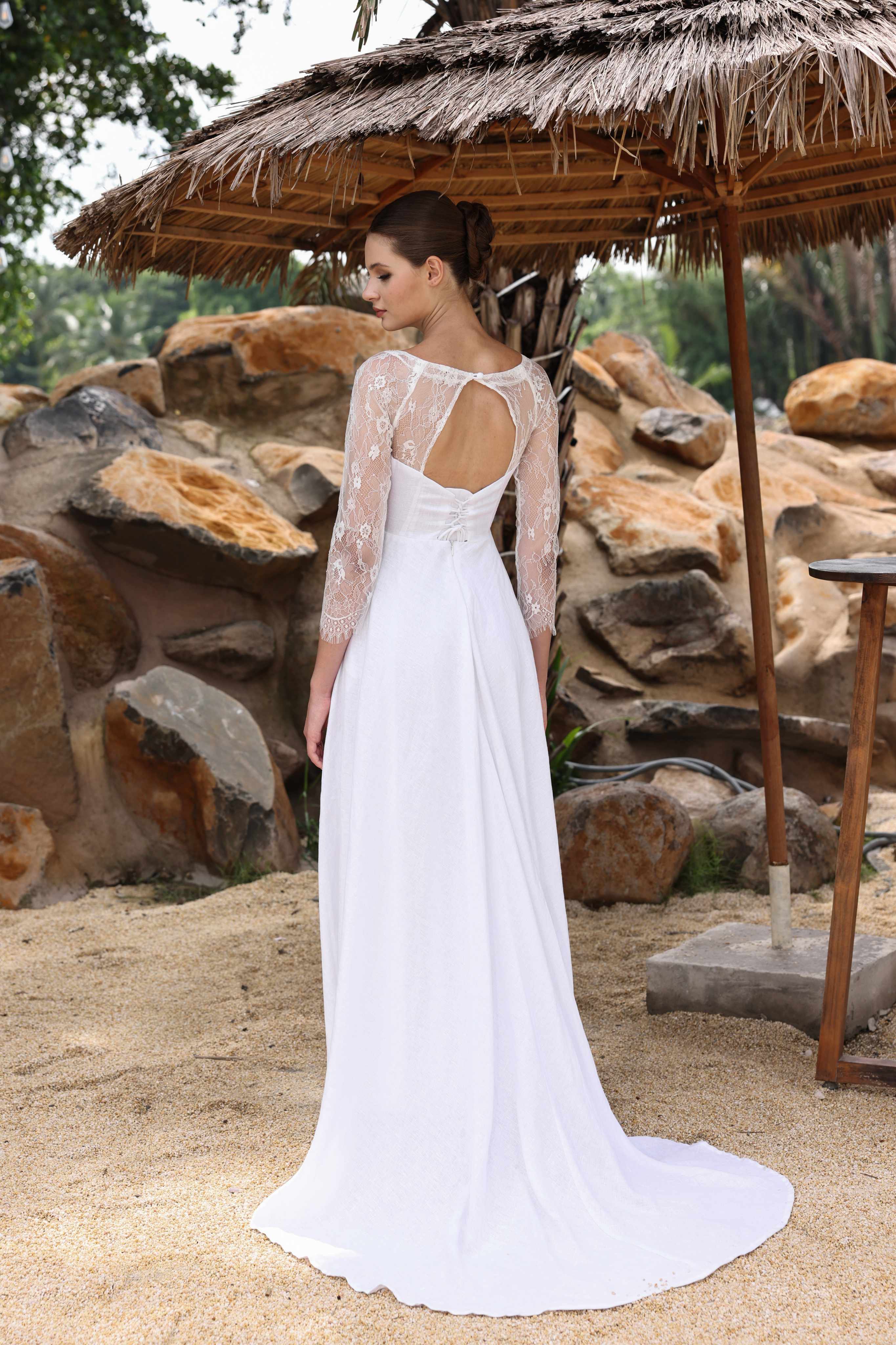 Woman in a white dress standing under a thatched umbrella with a stone wall background