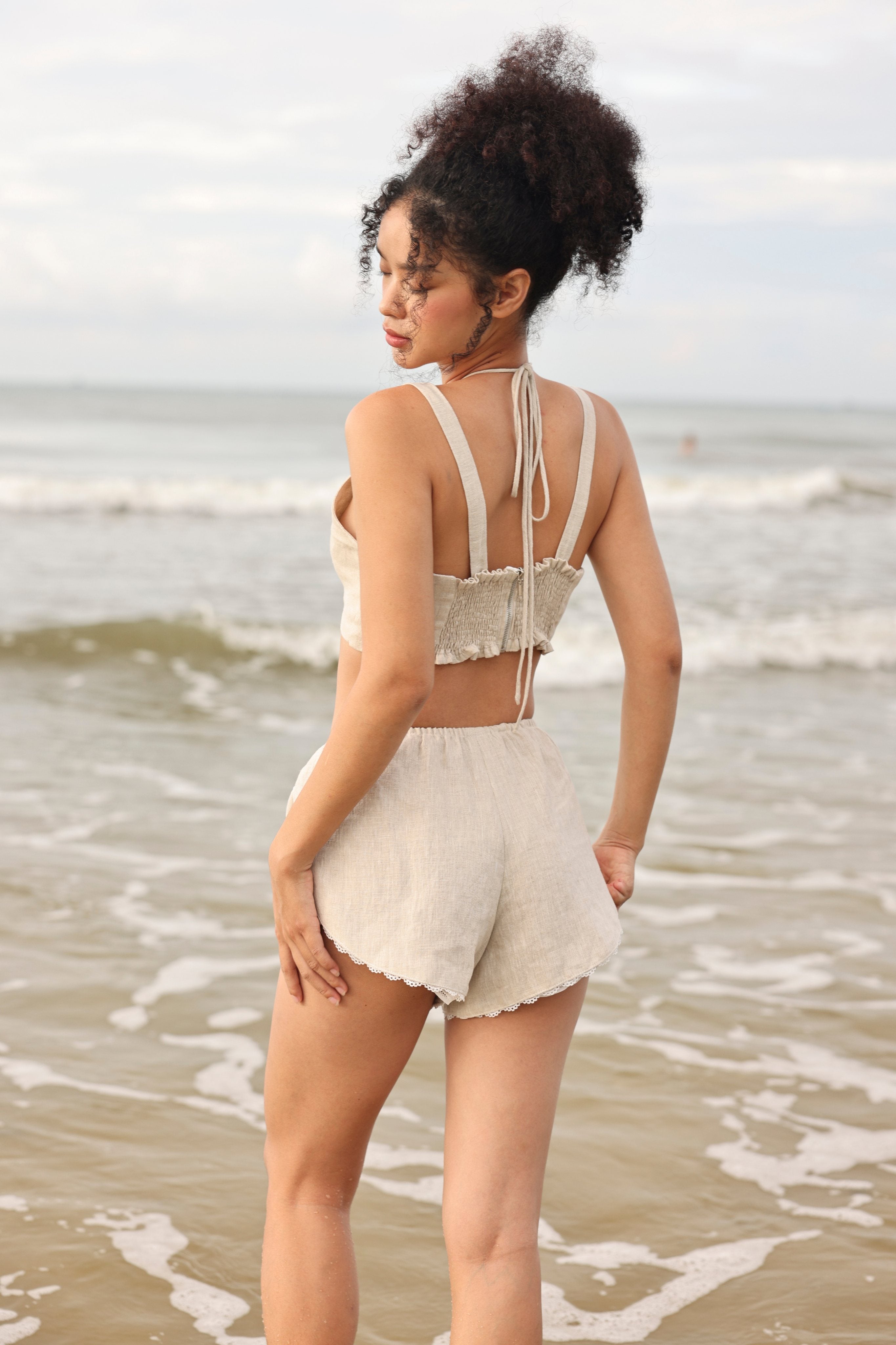Woman in a beige bikini standing on a beach with ocean waves in the background