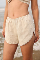 Beige lace-trimmed shorts worn by a person on a beach.