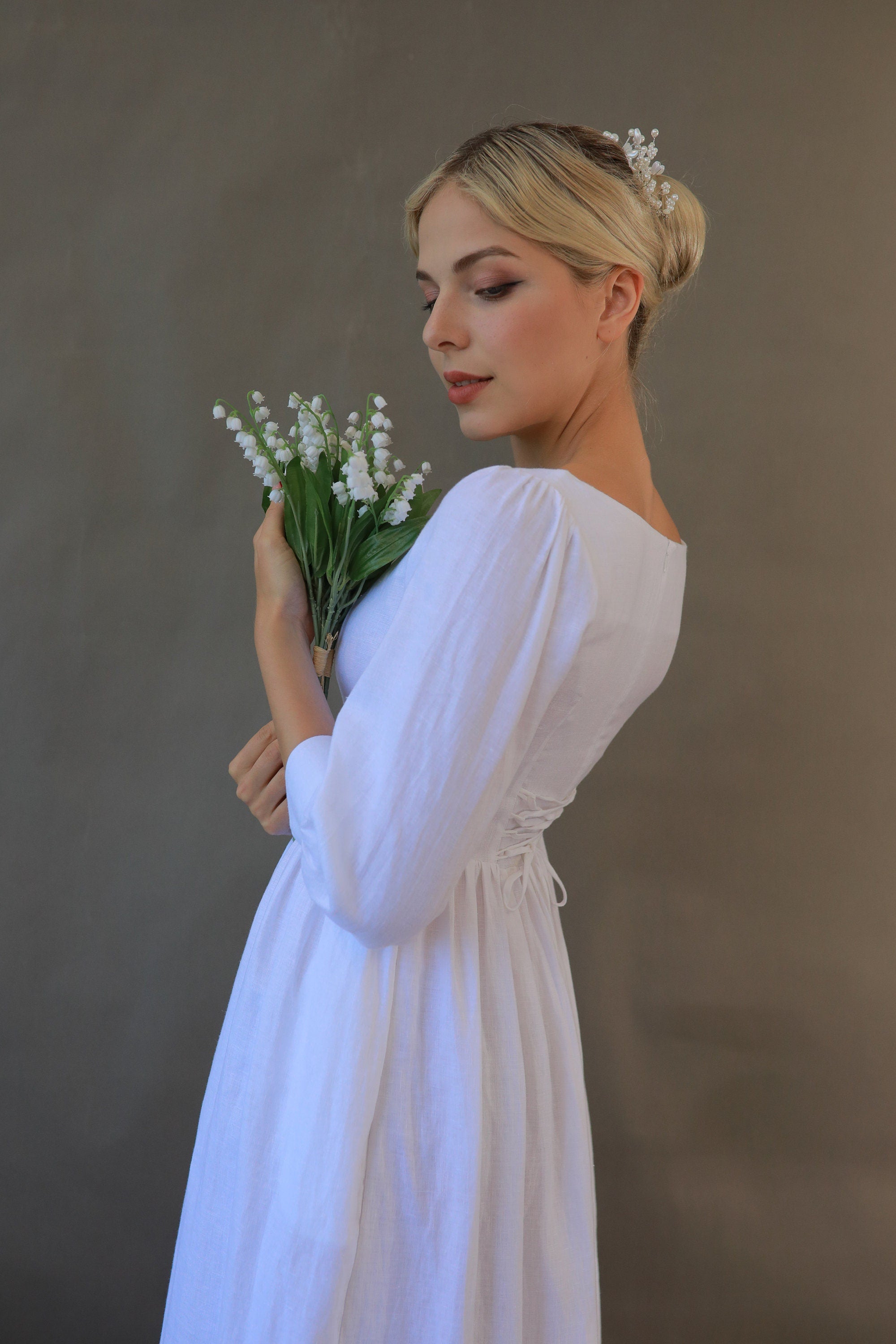 Woman in a white dress holding flowers against a plain background