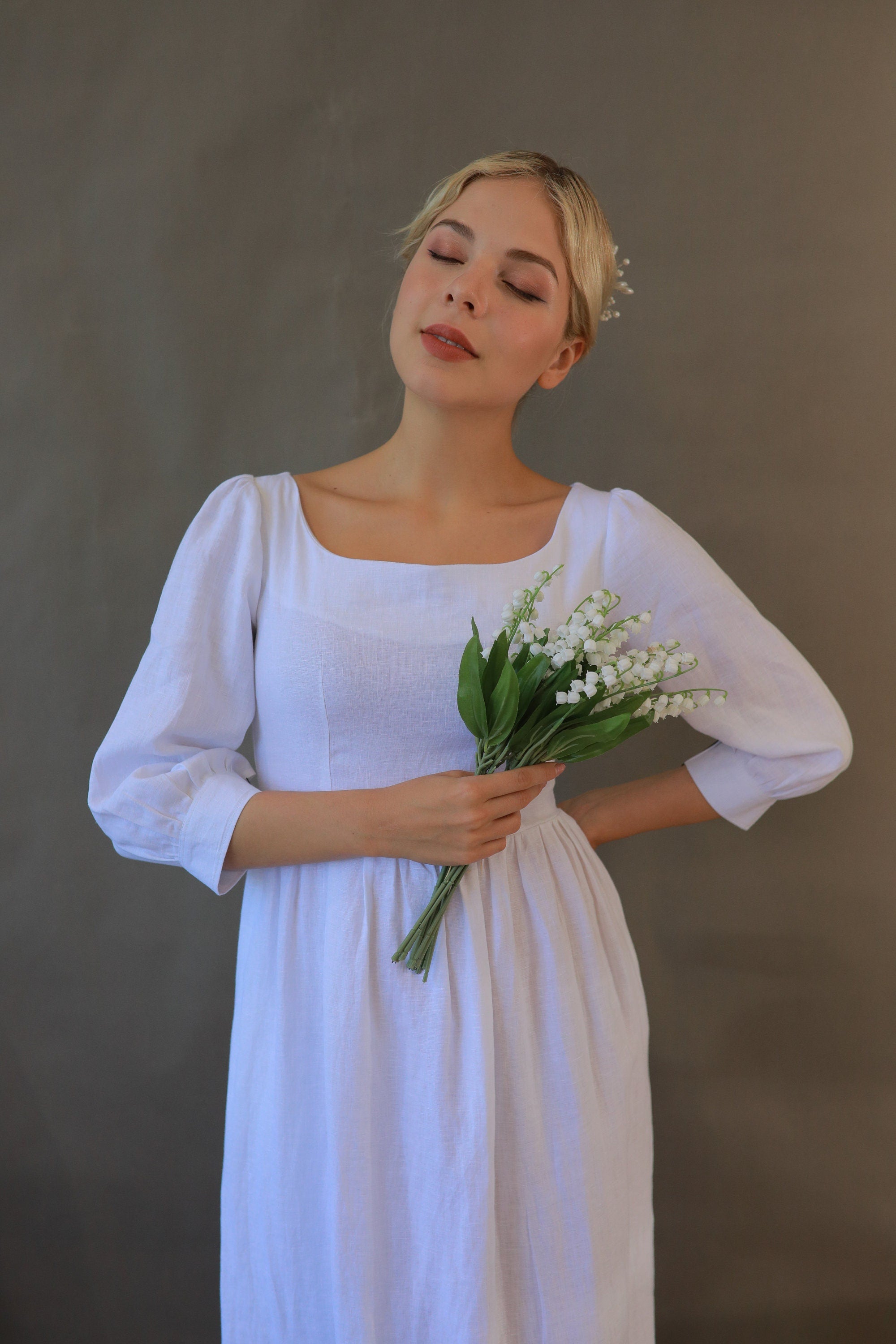 Woman in a white dress holding flowers against a plain background