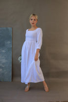 Woman wearing a white dress standing against a plain background