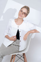 Woman wearing a white jacket with buttons, sitting on a modern chair against a white background