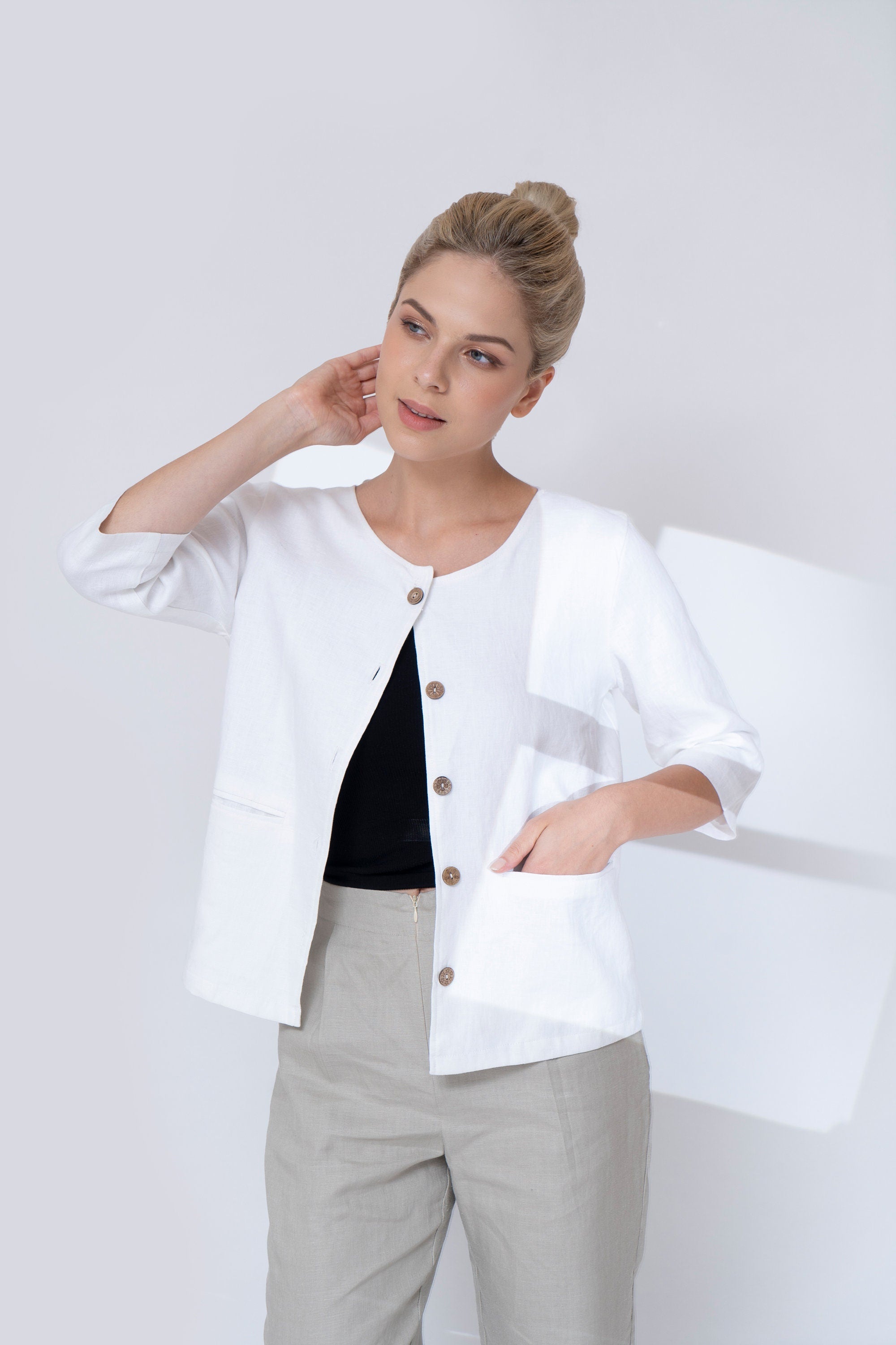 Woman wearing a white blazer with brown buttons on a plain background