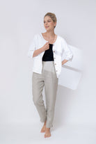 Woman wearing a white jacket, black top, and gray pants on a white background