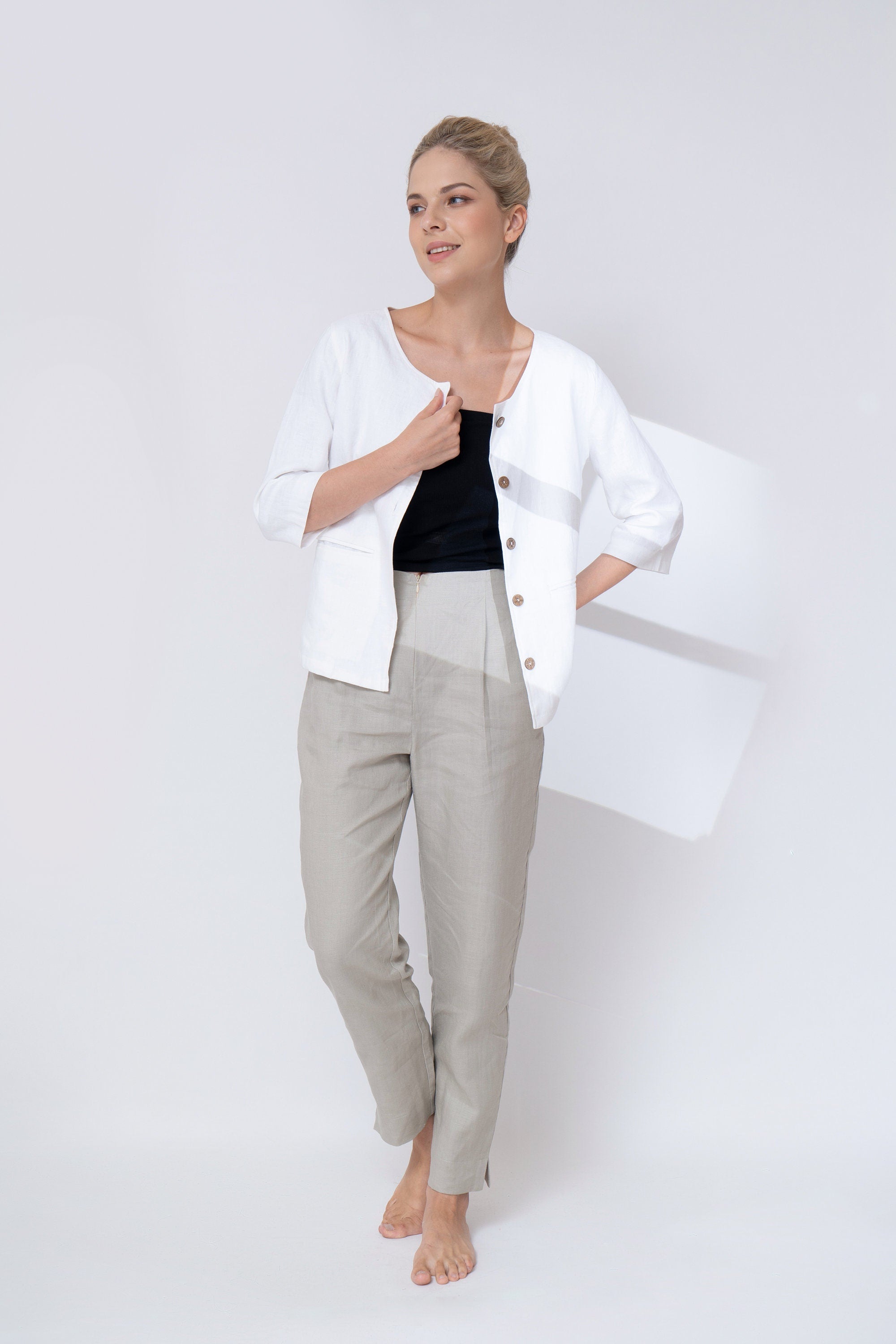 Woman wearing a white jacket, black top, and gray pants on a white background