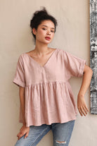 Woman wearing a pink blouse and jeans against a neutral wall.