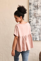 Woman wearing a pink blouse and blue jeans against a neutral wall.