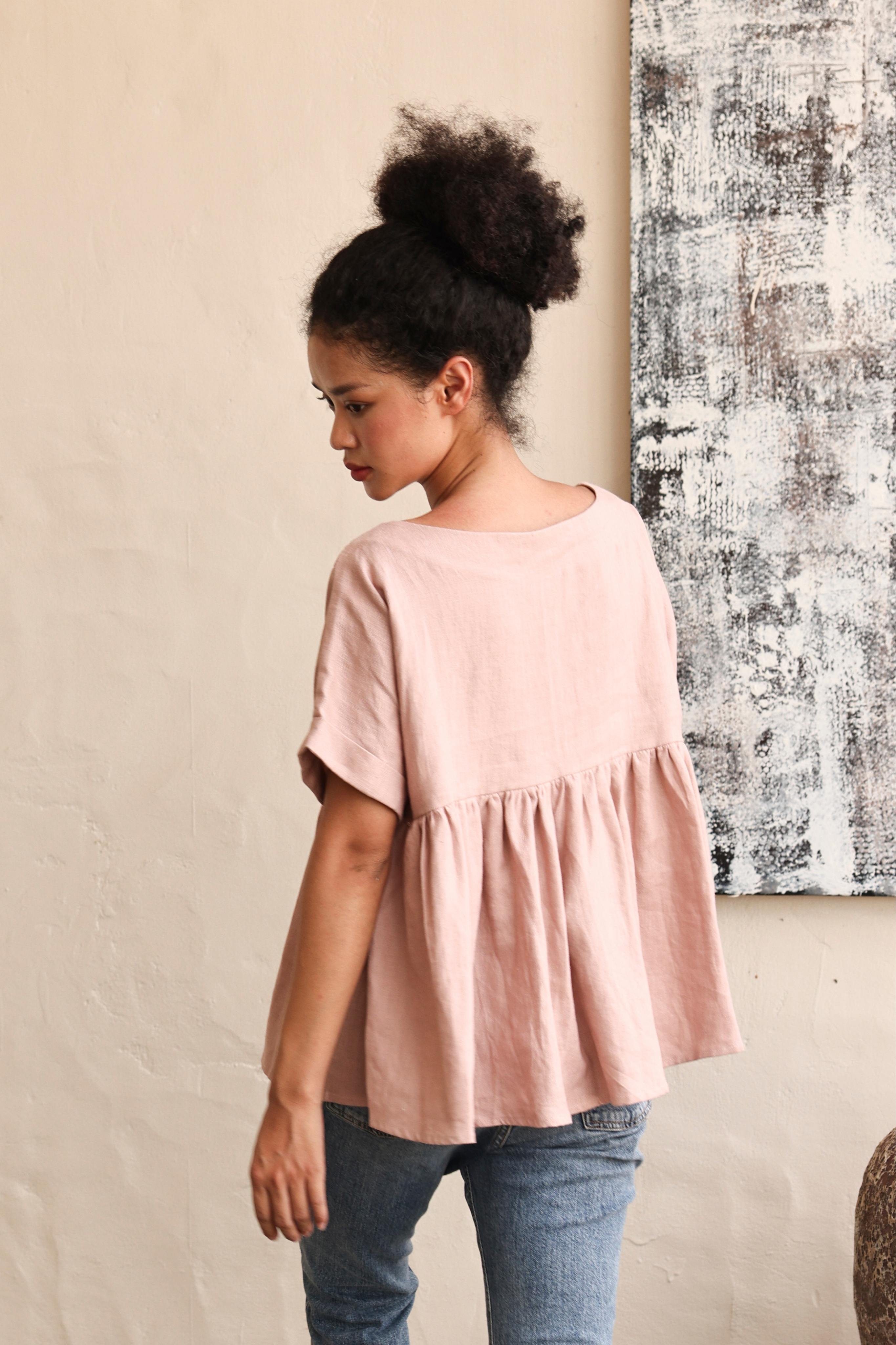 Woman wearing a pink blouse and blue jeans against a neutral wall.