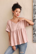 Woman wearing a pink blouse and blue jeans against a beige wall.