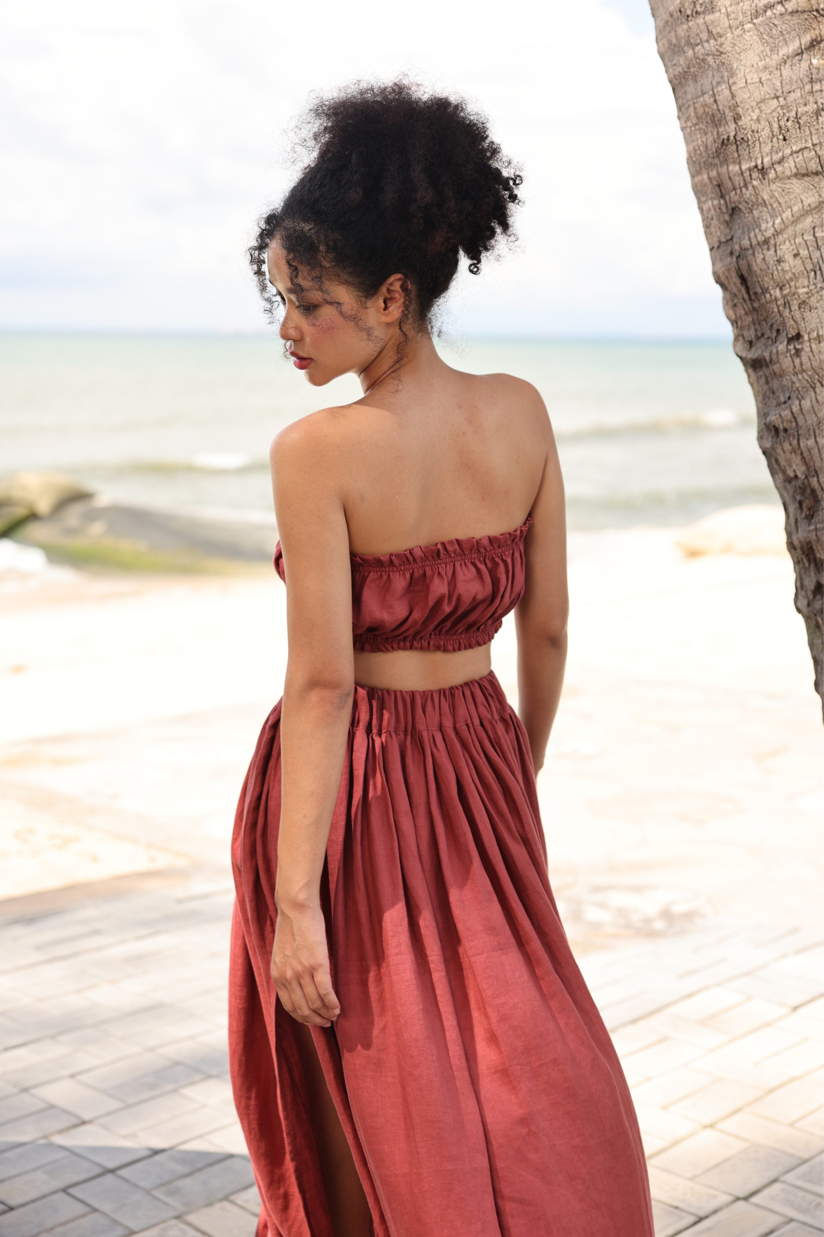 Woman in a rust-colored outfit standing on a beach with palm trees.