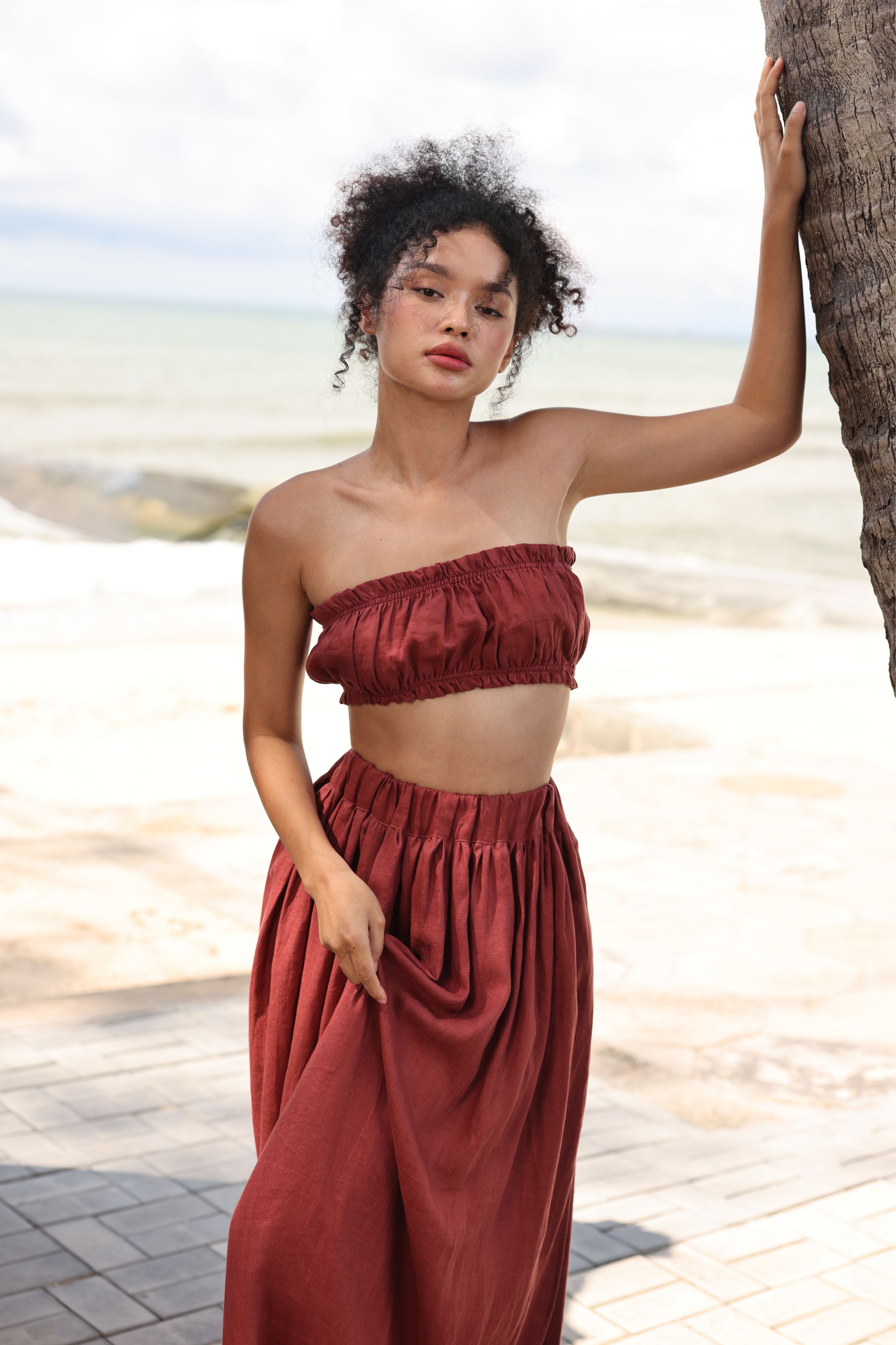 Woman in a red outfit standing on a beach with palm trees.