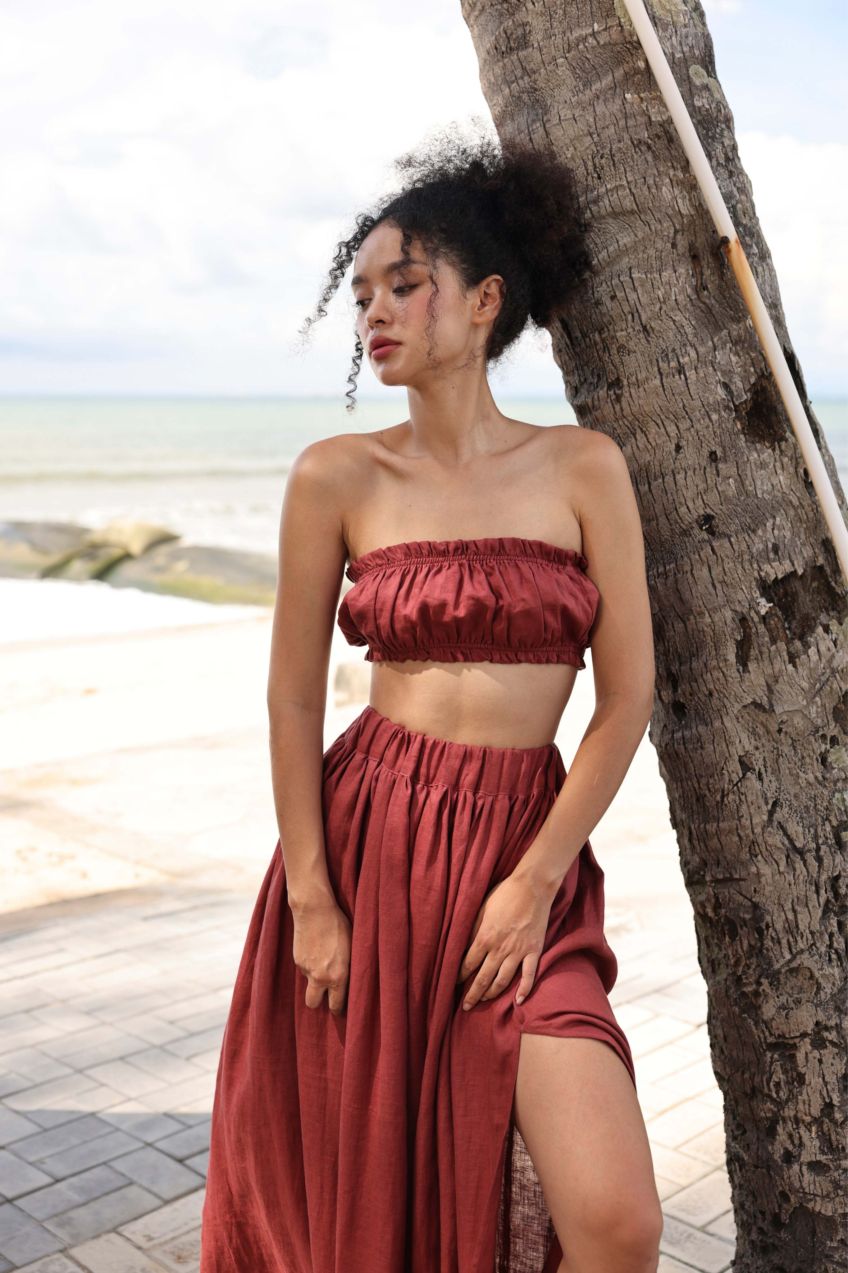 Woman in a red outfit standing by a palm tree on a beach.