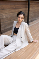 Woman in a white blazer and black top sitting on a wooden floor.