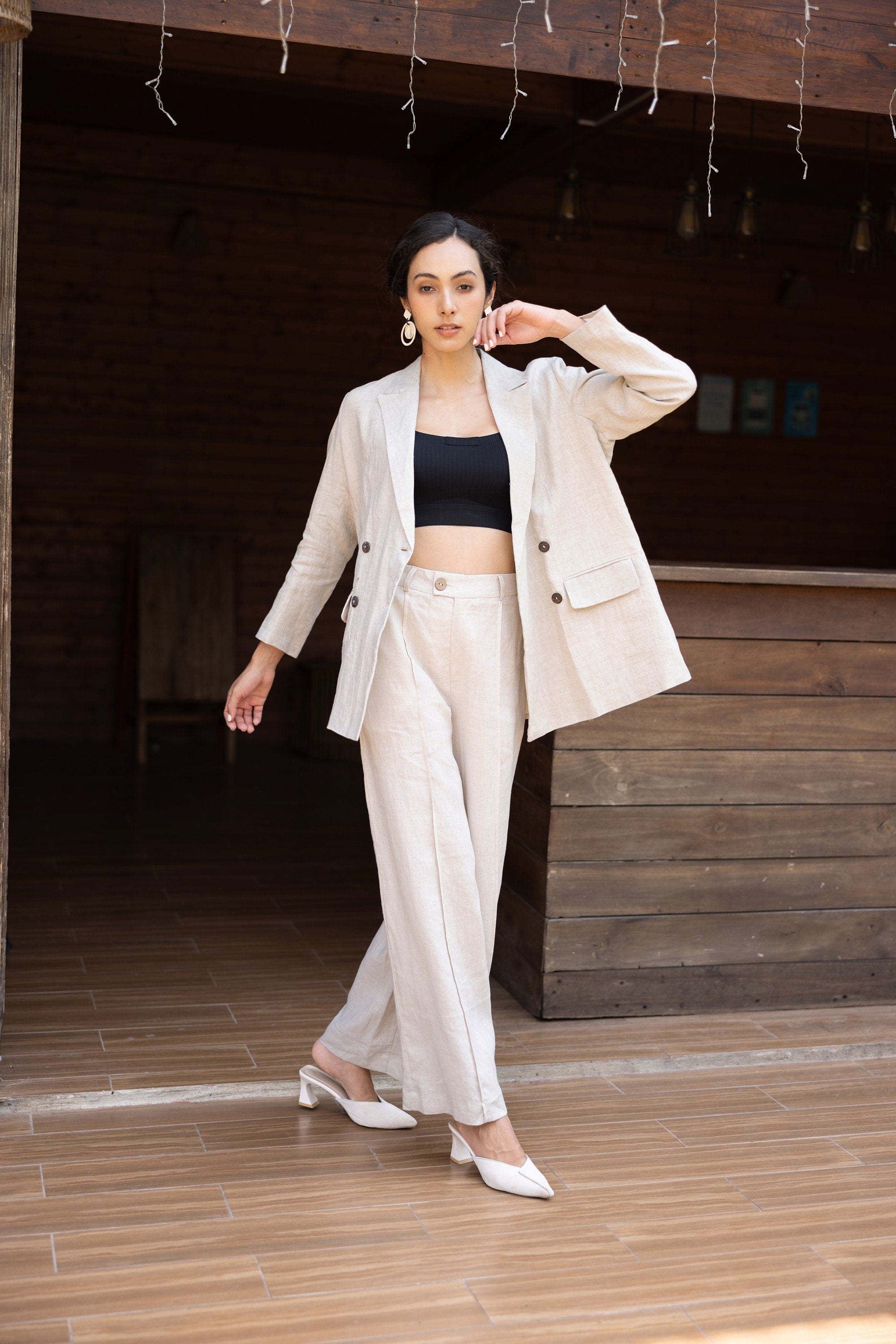 Woman in a beige blazer and pants with a black top, standing in a wooden interior setting.