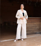 Woman in a beige suit standing in a room with wooden floor and walls.
