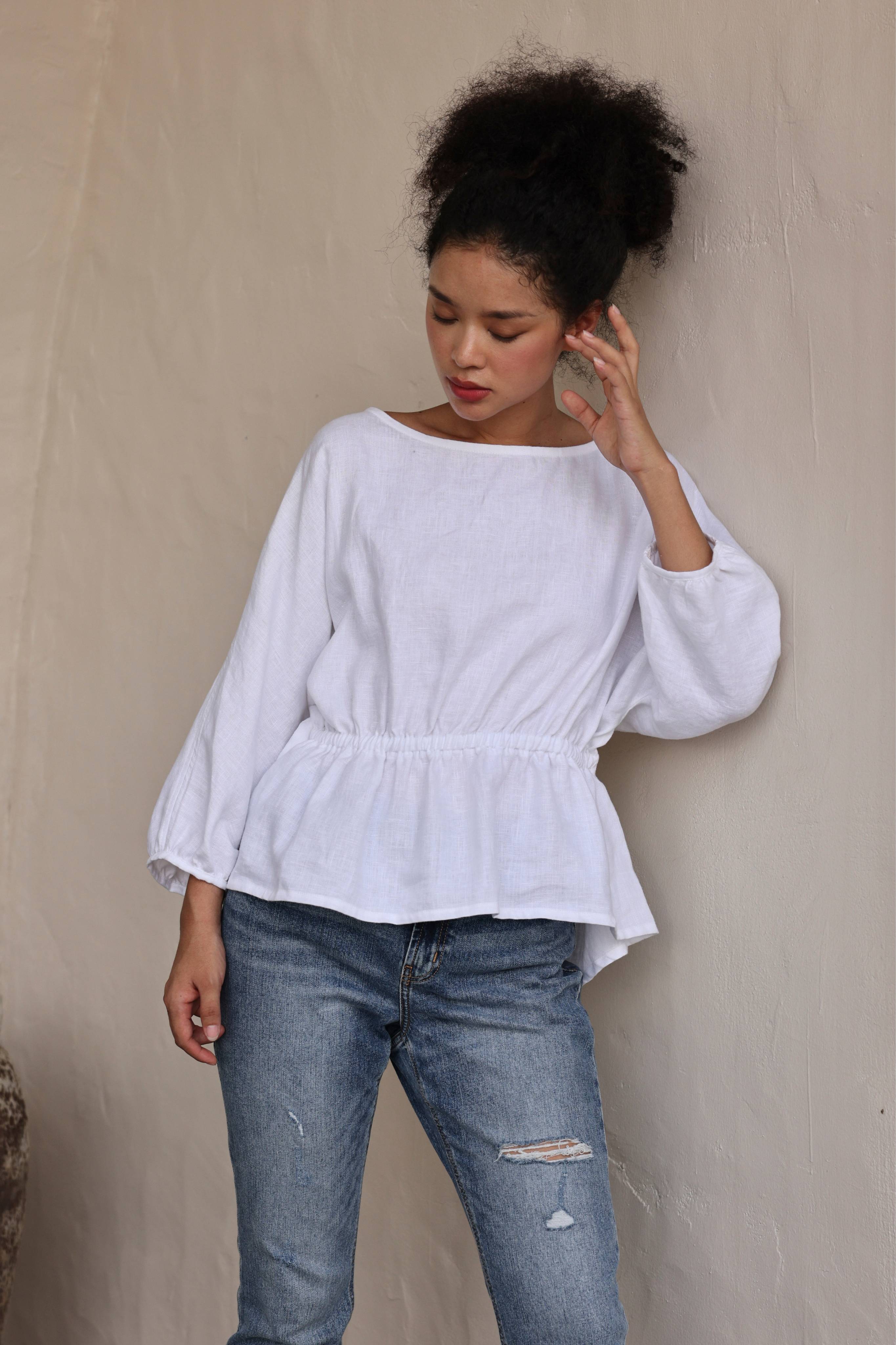 Woman wearing a white blouse and blue jeans against a beige background