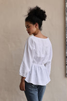 Woman wearing a white blouse and blue jeans against a beige wall